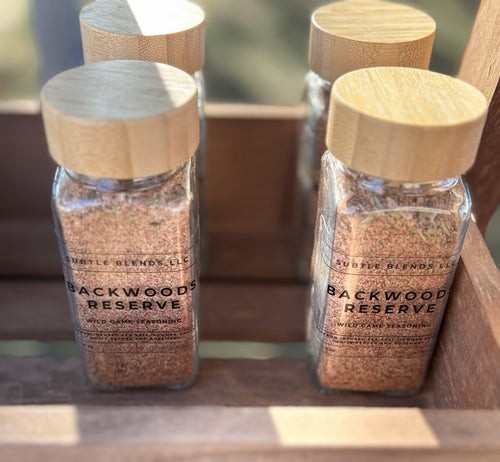 Three glass jars with wooden lids labeled 'Backwood Reserve' on a wooden surface.
