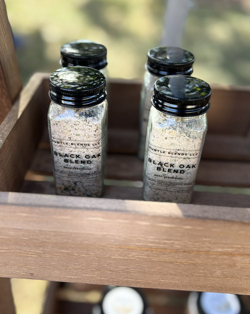 Four small bottles labeled 'Black Oak Blend' on a wooden surface with a blurred natural background.