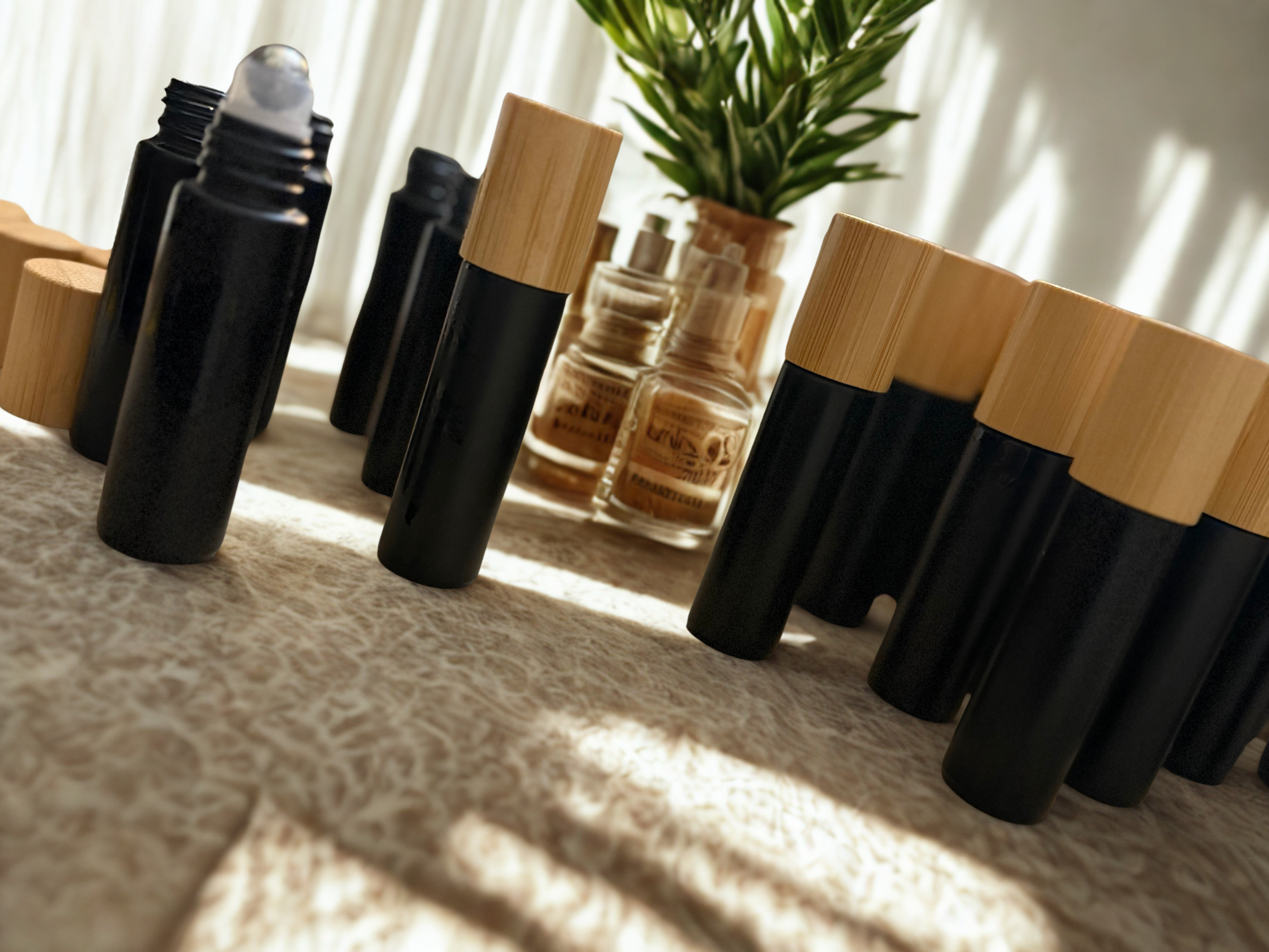 Set of black and wooden roller bottles on a textured surface with a plant in the background.