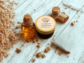 Bottle of oil and jar of balm on a wooden surface with dried herbs.