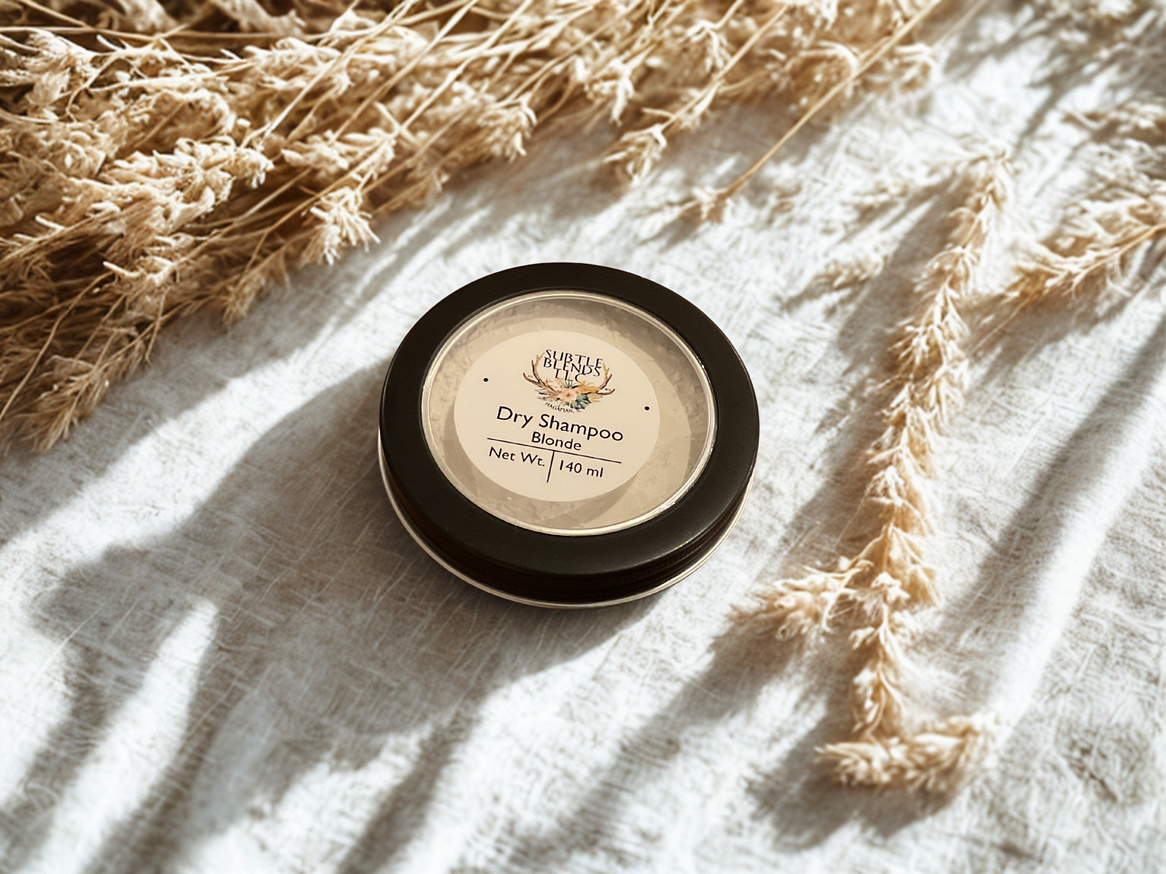 Dry shampoo container on a textured surface with dried plants