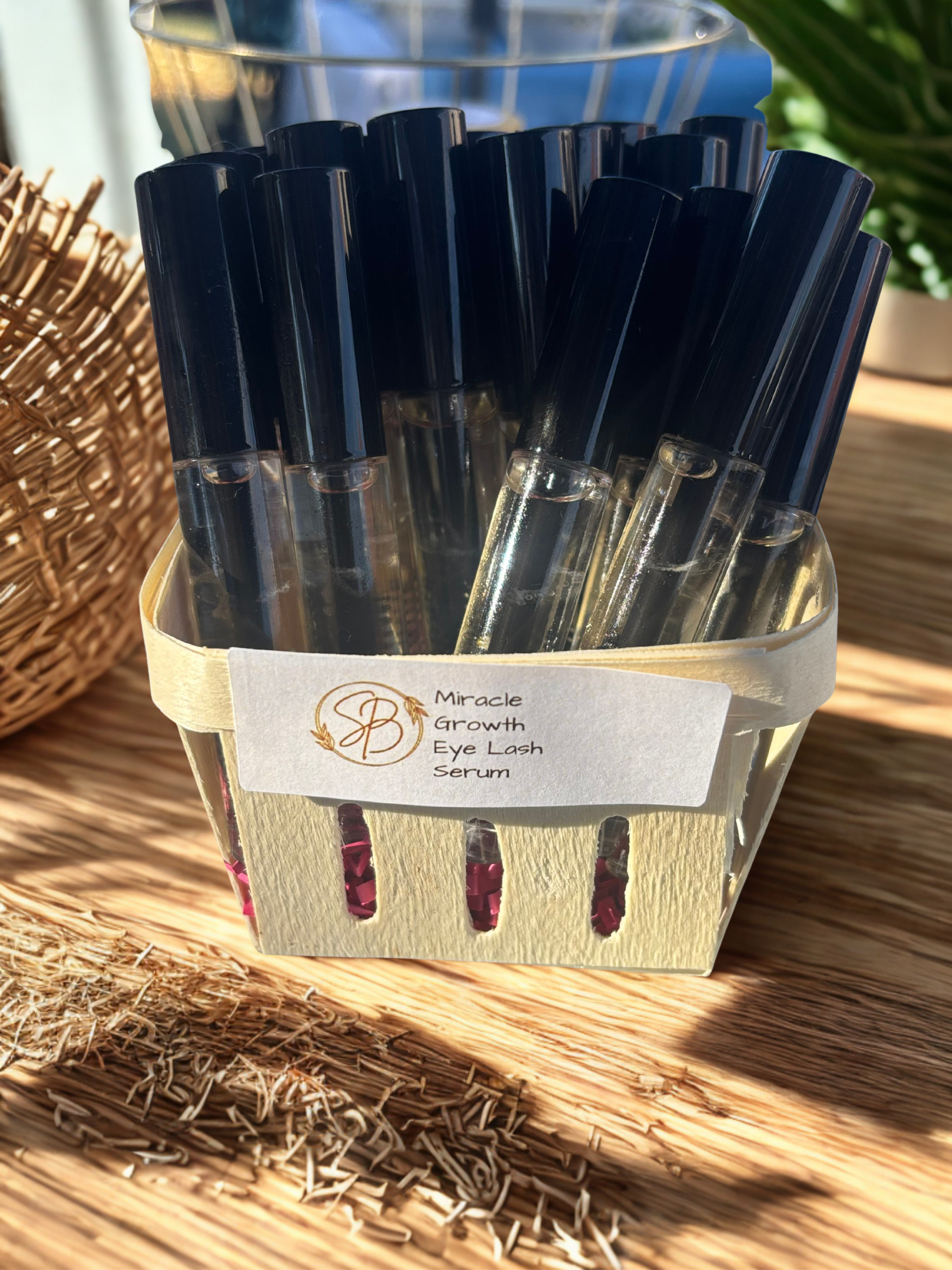 Collection of eye lash serum bottles in a wooden basket on a wooden surface.