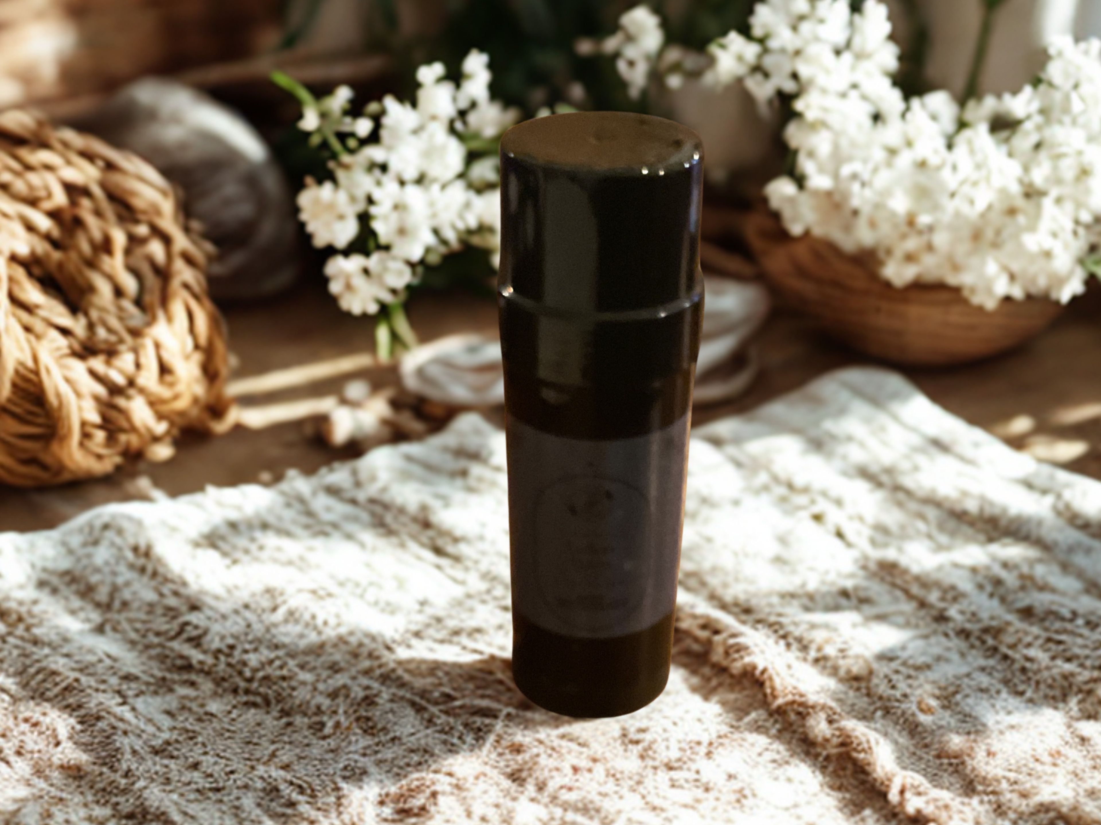 Black cylindrical container on a textured surface with flowers in the background