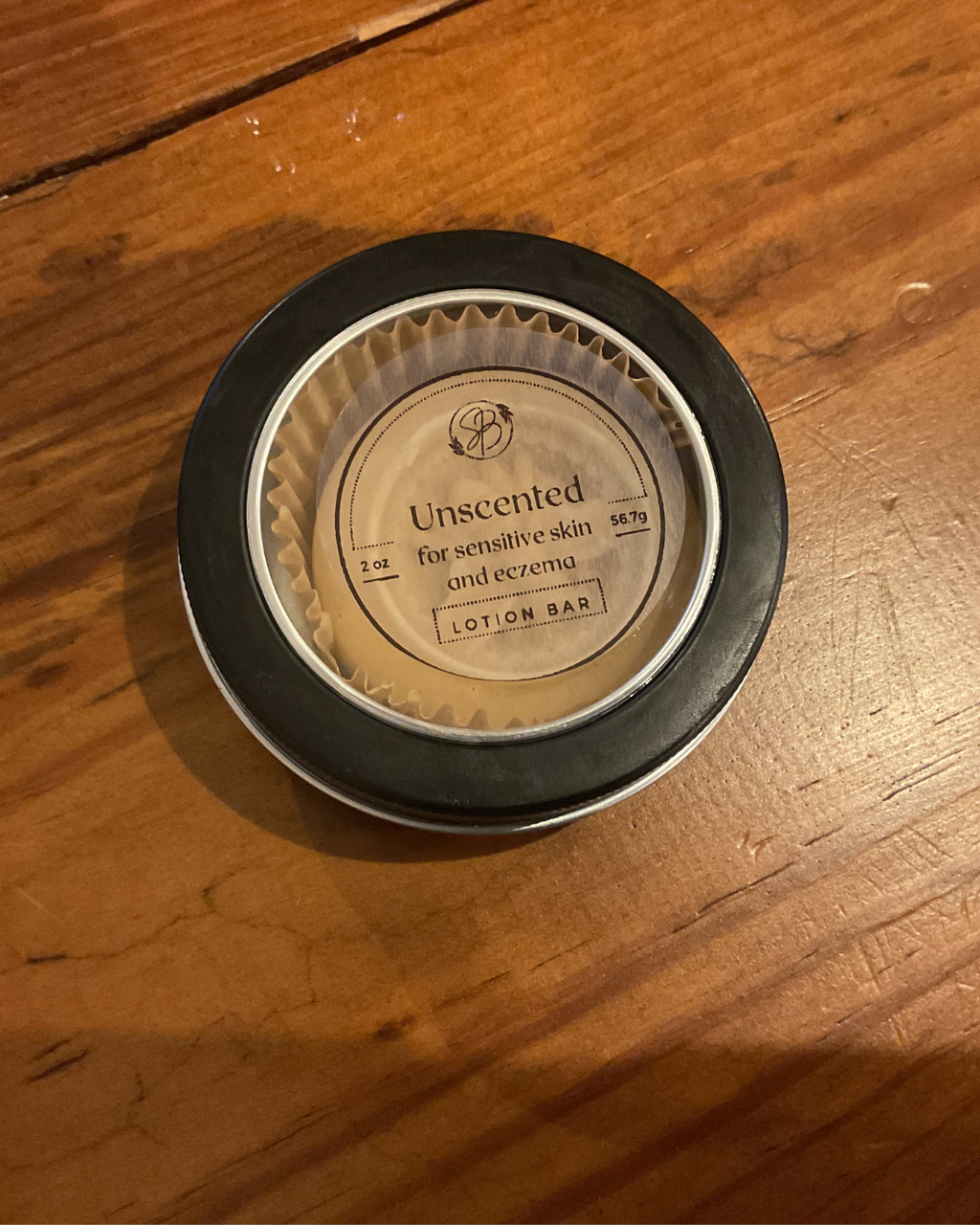 Unscented lotion bar in a black container on a wooden surface