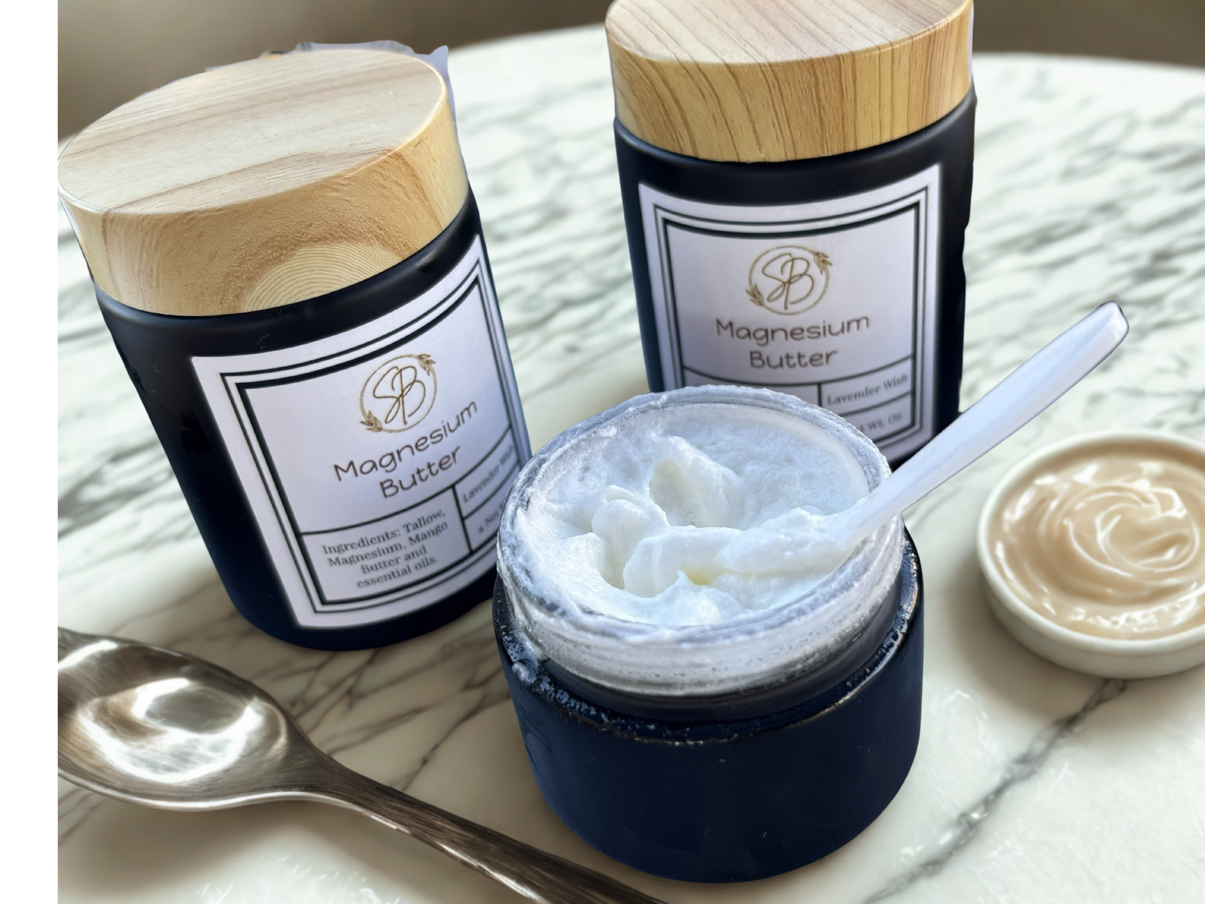 Jars of magnesium butter on a marble surface with a spoon and small dish.
