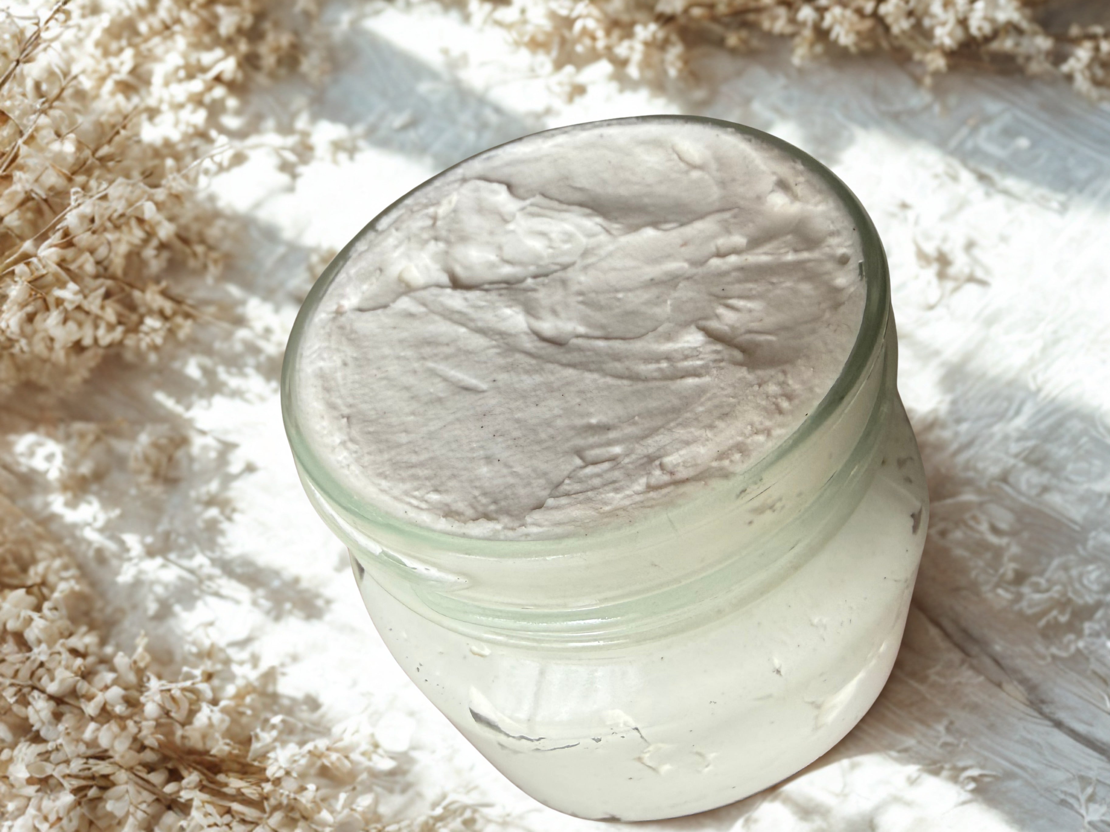 Jar of white cream on a textured surface with dried flowers